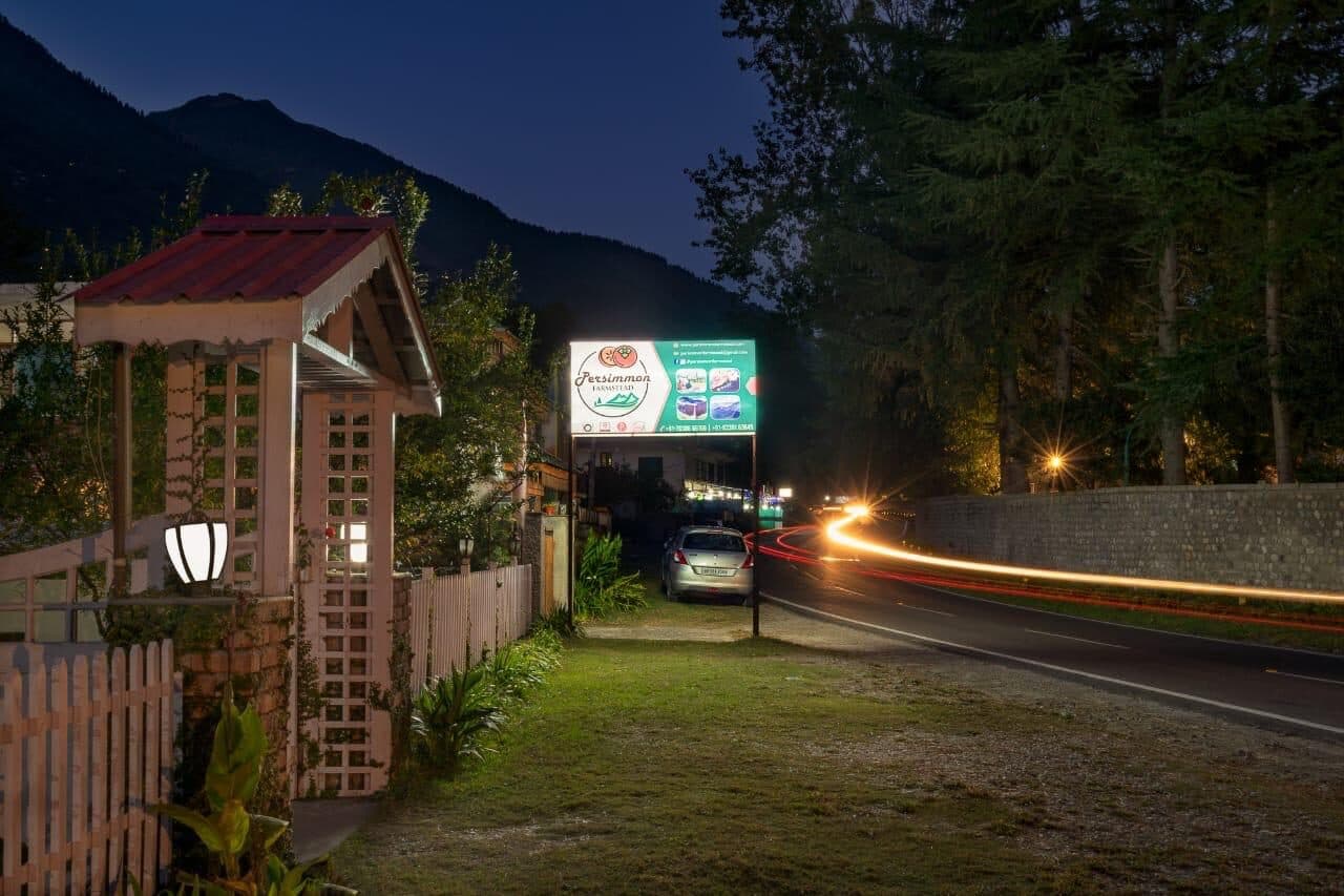 The farmstead lit at night, a car's light trail on the highway