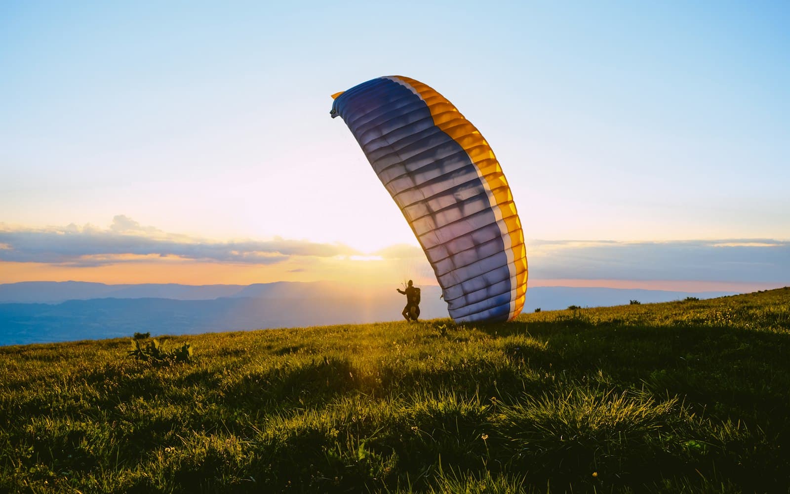 A tandem paraglider turning over the green slopes of Solang Valley on a clear morning, snow peaks in the distance